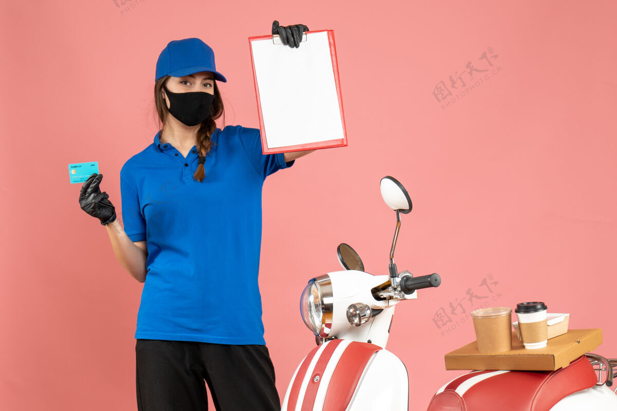 手套正面图：戴着医用面罩手套的快递女孩站在摩托车旁边 摩托车上放着咖啡蛋糕 手里拿着粉色背景的文件和银行卡摩托车人桃