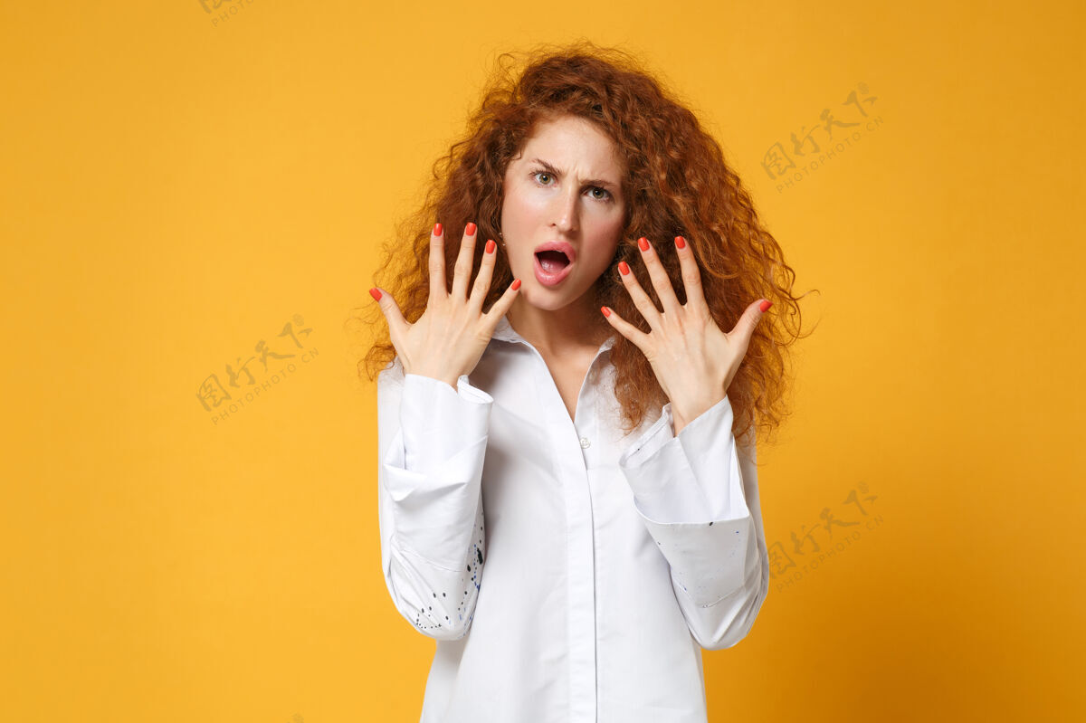 成人震惊的年轻红发女子穿白衬衫的女孩在黄橙色的墙上摆出孤立的姿势衬衫手势一个