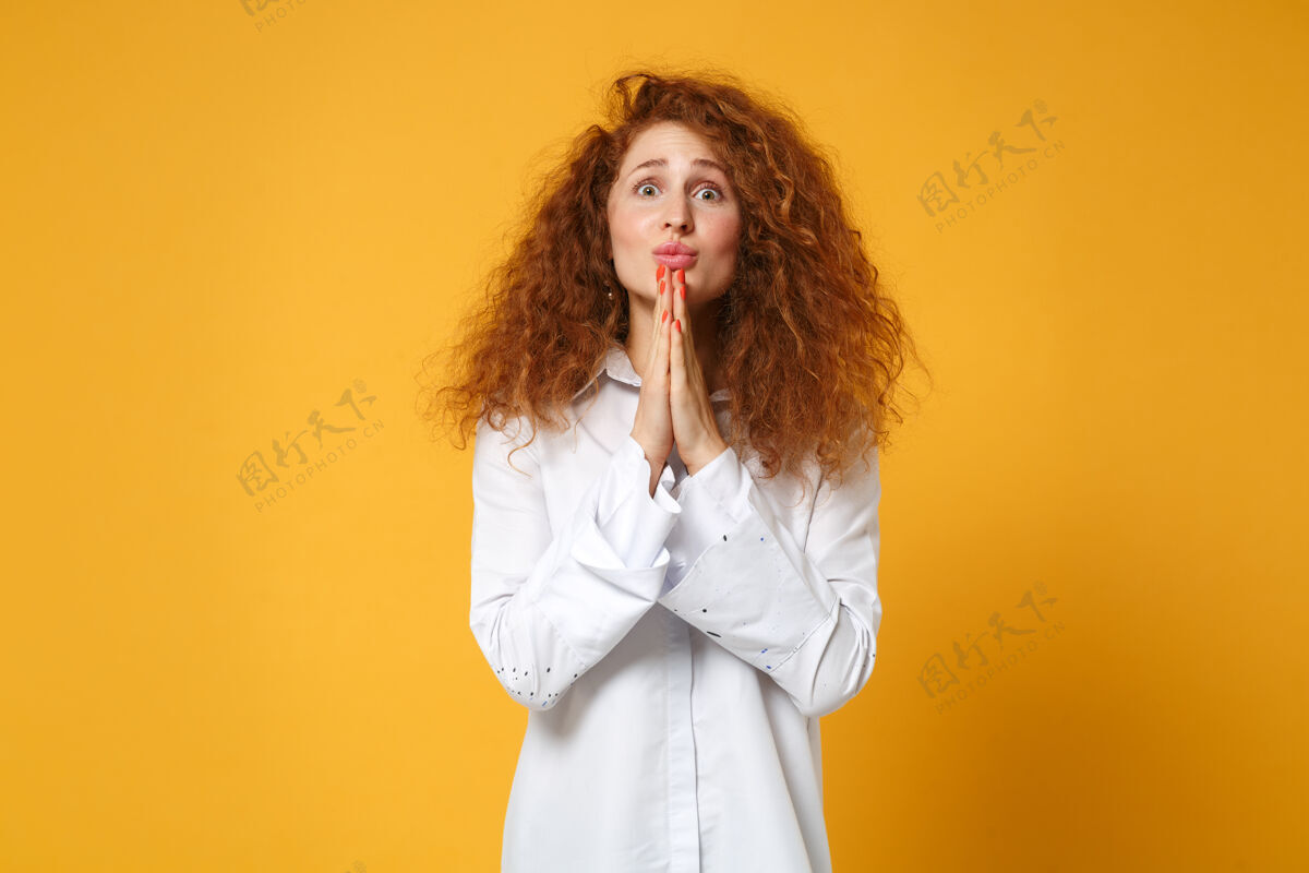 人穿着休闲白衬衫的年轻红发女郎在黄橙色的墙上孤零零地摆姿势白种人卷曲一个