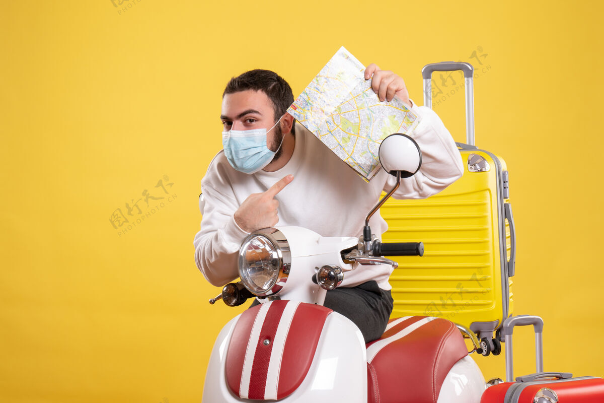 手提箱旅行概念的俯视图 戴着医用面罩的年轻人站在摩托车旁边 黄色手提箱放在上面 拿着地图感到好奇年轻人旅行感觉