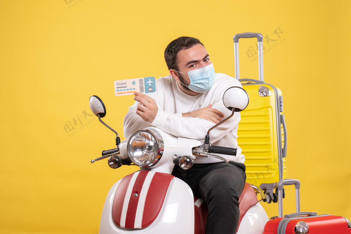 面具旅行概念的俯视图 戴着医用面罩的年轻人坐在摩托车上 黄色手提箱放在上面 拿着车票 感觉很惊讶人顶男