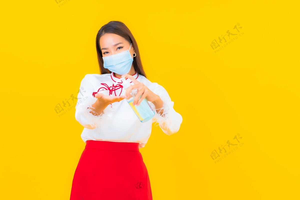护理肖像美丽的亚洲年轻女子戴上口罩 用酒精凝胶保护黄色的covid19流行病污染办公桌