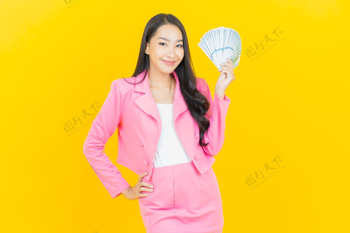 财务肖像美丽的亚洲年轻女子微笑着在黄色的墙上有很多现金和金钱赢家立场现金