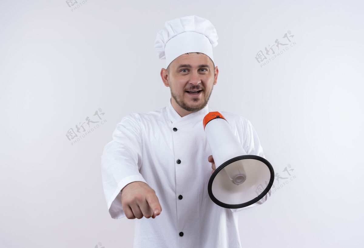 拿着快乐的年轻帅哥厨师身着厨师制服 手持扬声器 孤立地指着白墙上帅气烹饪年轻
