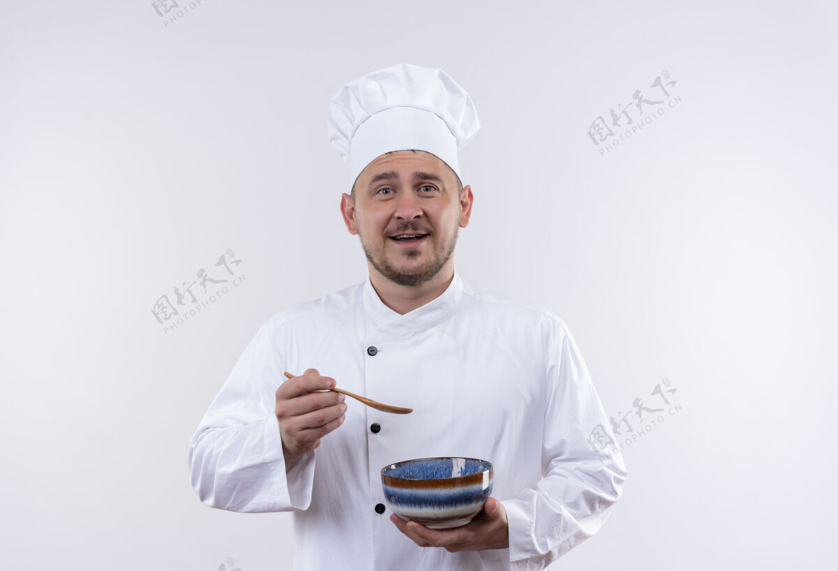 厨师快乐的年轻帅哥厨师穿着厨师制服拿着碗和勺子在隔离的白色墙壁上复制空间勺子快乐制服