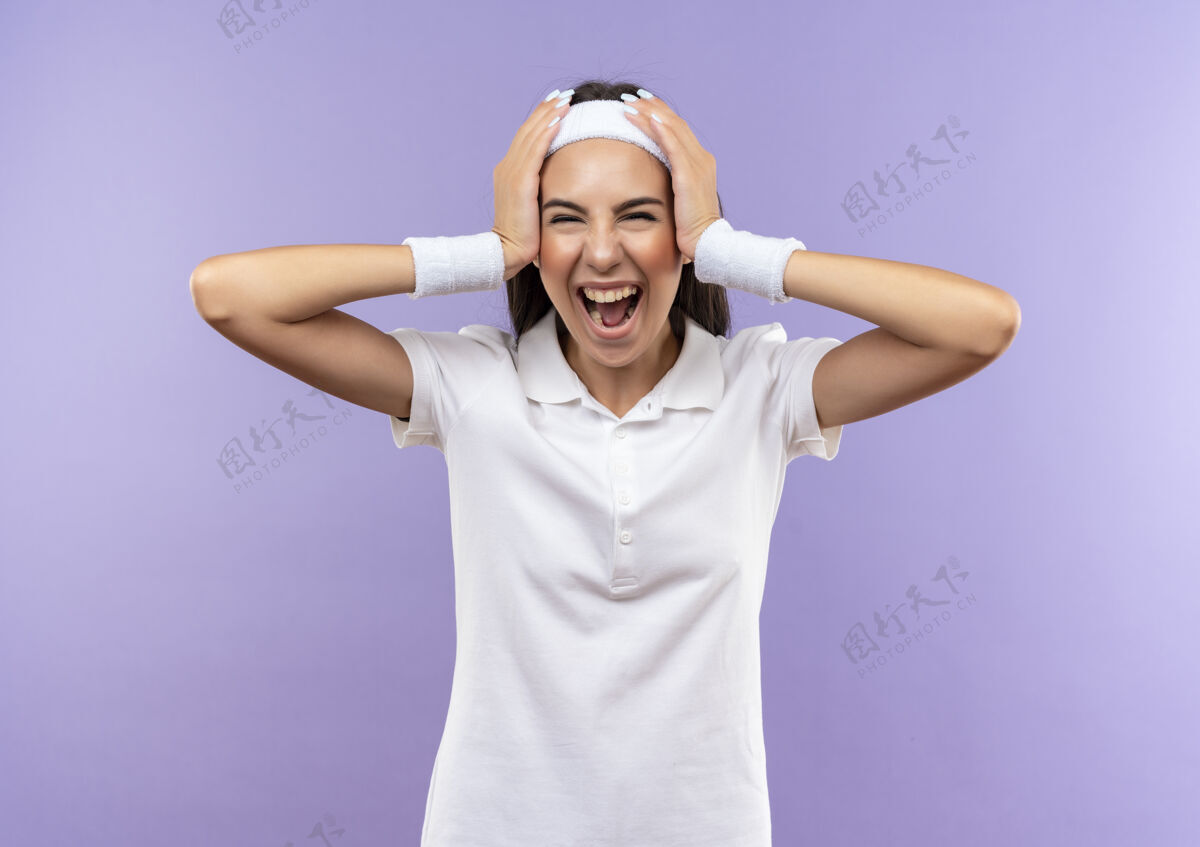 头快乐漂亮的运动女孩戴着头带和腕带把手放在头上隔离在紫色的墙上手运动头带