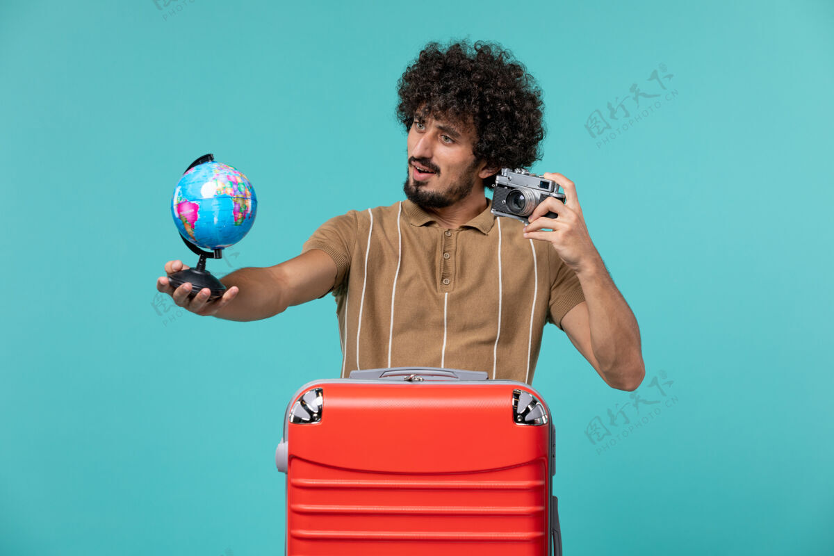 航行度假的男人拿着浅蓝色的小地球仪和照相机地球仪旅行风景