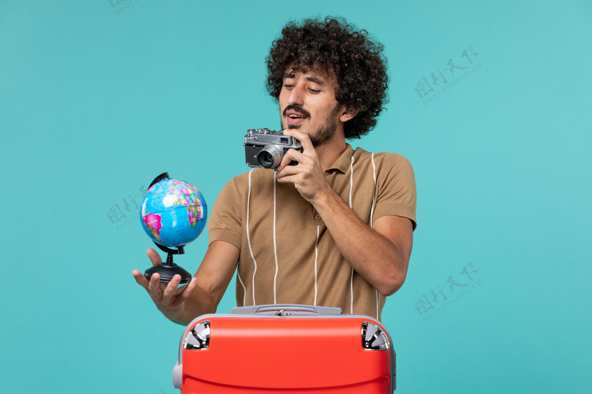 成人度假的男人拿着小地球仪和相机在蓝色的天空上拍照举行人物地球仪