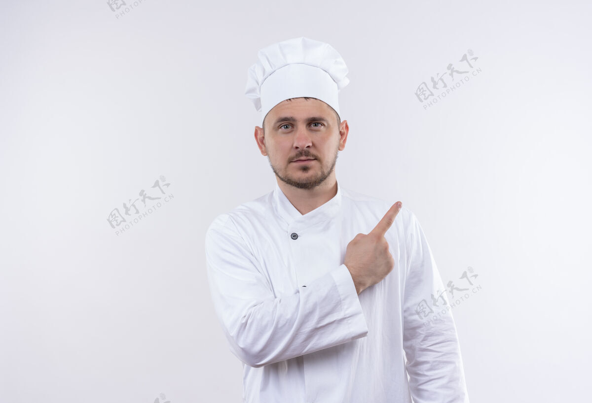 帅气自信的年轻帅哥厨师身着厨师制服指着隔离在白色墙上的一侧指点自信侧身