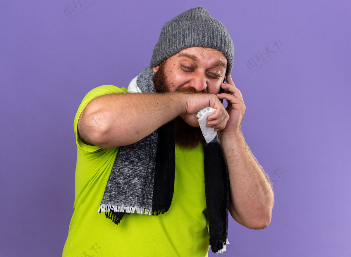 手机戴着帽子 围着暖和的围巾 留着不健康的胡须 脖子上戴着暖和的围巾 感觉很可怕 患流感 打手机 流鼻涕 站在紫色的墙上打喷嚏周围吹跑步