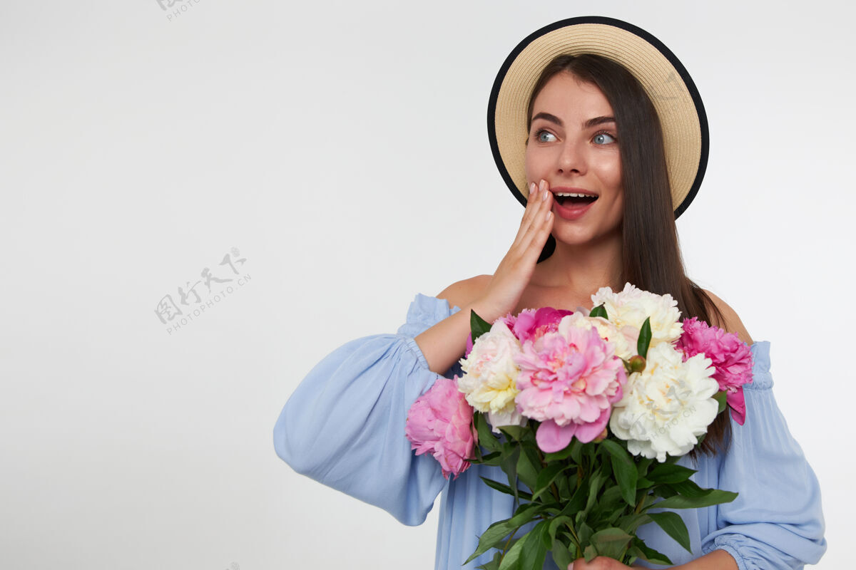 面部快乐的女人 深色长发 戴着帽子 穿着蓝色的裙子 捧着一束鲜花 抚摸着她的脸颊 惊讶不已深色脸爱情
