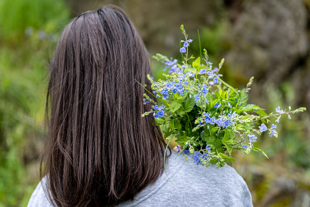 开花女孩拿着春天森林里收集的一束花 从后面看成人女人绿色