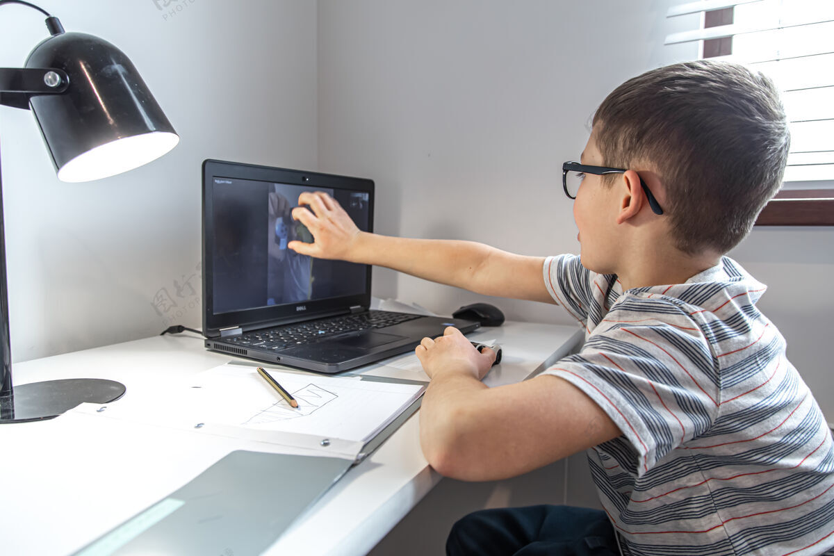 教育一名小学生坐在笔记本电脑前的书桌旁 在家里通过视频链接与朋友在线交流笔记本电脑在线学校桌子
