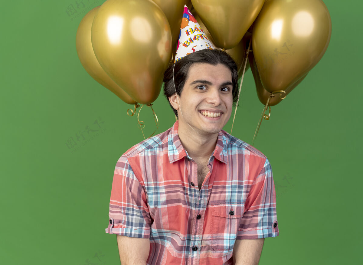 空间笑容可掬的高加索帅哥戴着生日帽站在氦气球前看着镜头帽子站男人