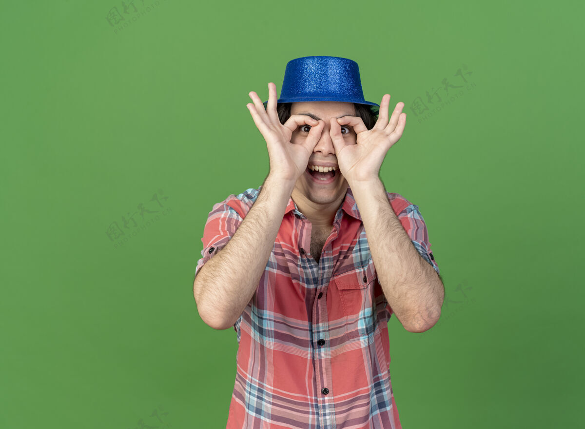 蓝色戴着蓝色派对帽的白人帅哥兴奋地用手指看着镜头复制穿过绿色