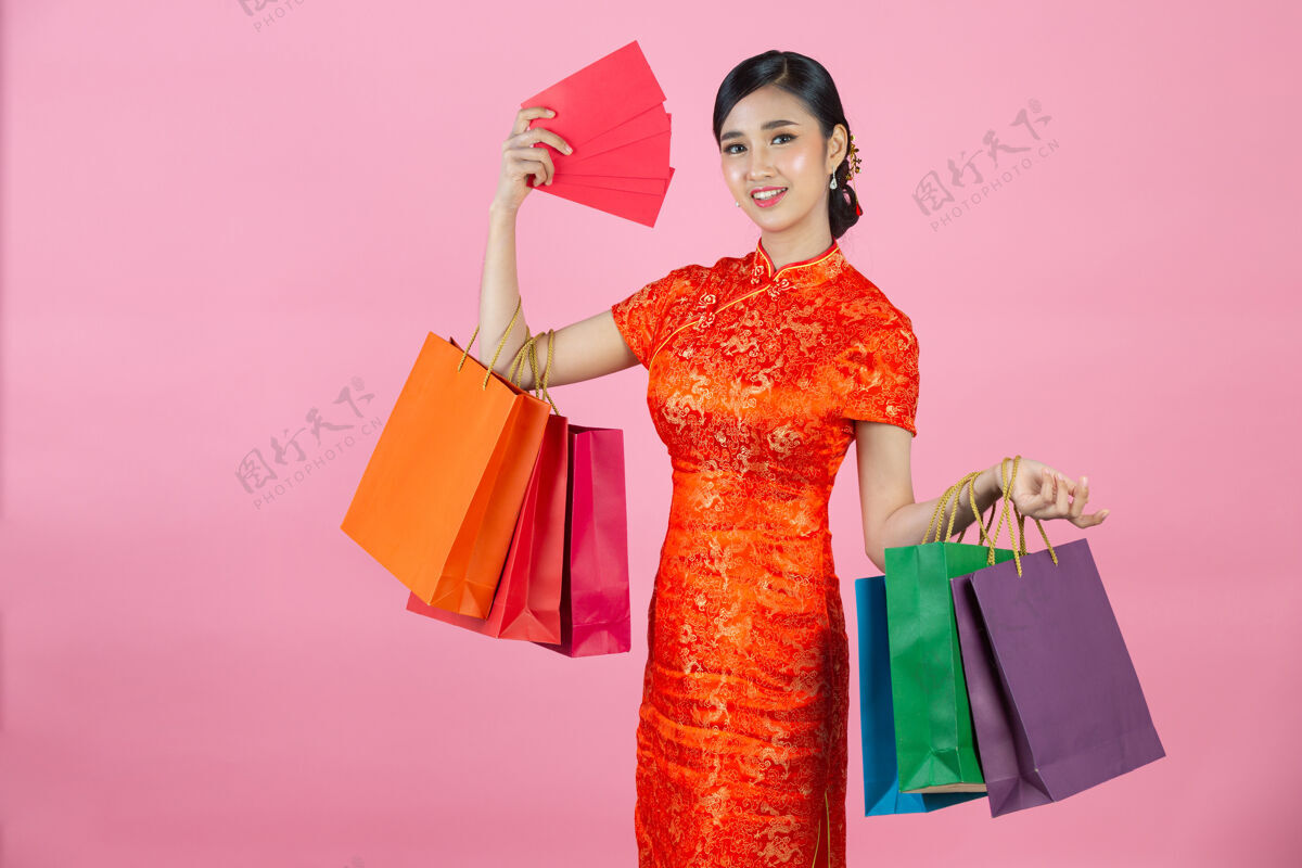 展示美丽的亚洲女人快乐的微笑和购物在中国新年的粉红色背景亚洲人红色女人