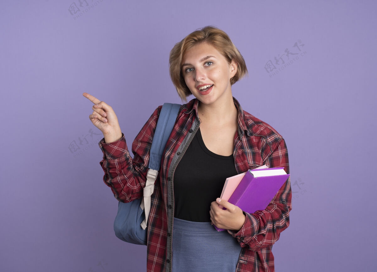 背包快乐的年轻斯拉夫学生女孩背着书包 把书和笔记本放在一边举行女孩紫色