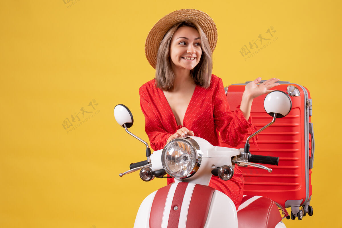 漂亮女孩骑着轻便摩托车的漂亮女孩 红色手提箱指向右边右边指成人