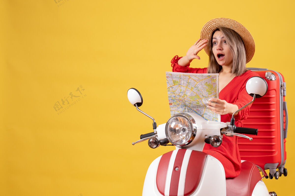 派对骑着轻便摩托车的漂亮女孩拿着红色的手提箱拿着地图招呼着某人某人红色地图