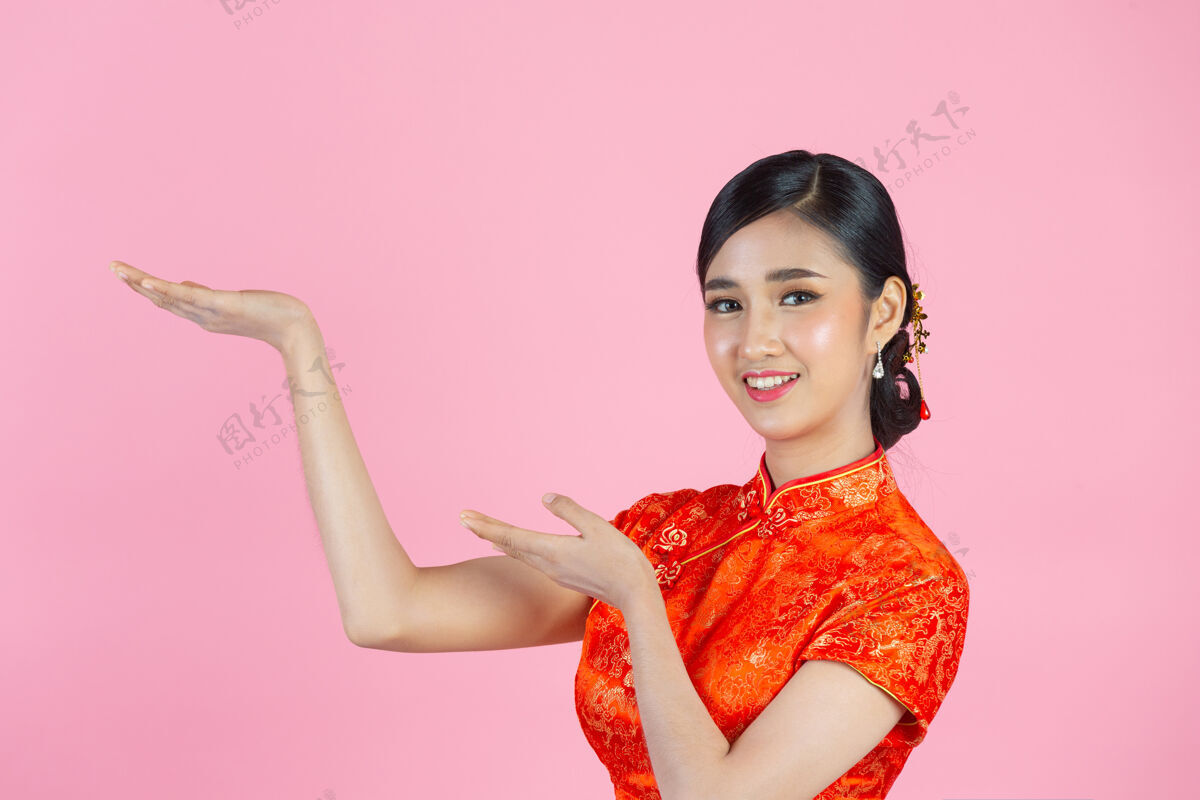 微笑美丽的亚洲女人快乐的微笑 在中国新年的粉红色背景上向你展示一些东西中国人文化女孩