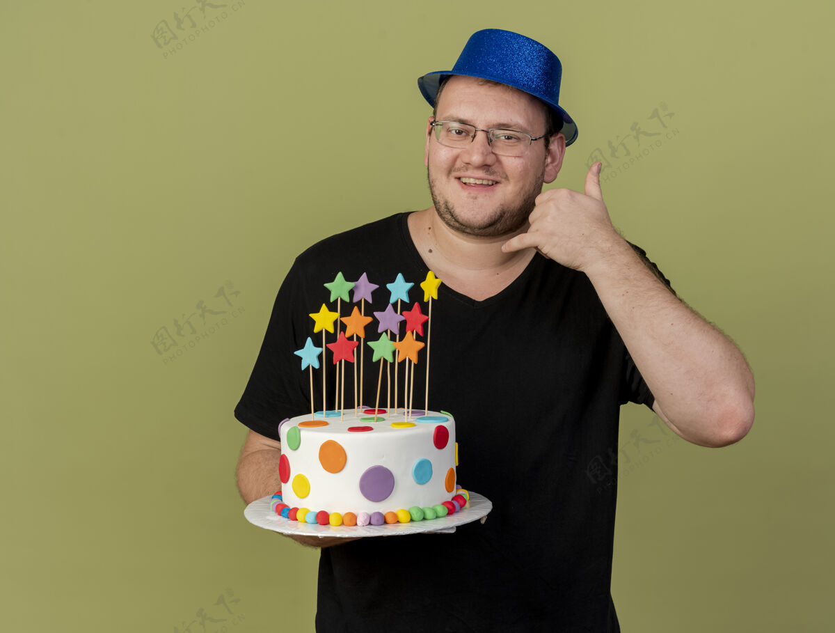 复制微笑的成年斯拉夫人戴着眼镜 戴着蓝色的派对帽 拿着生日蛋糕 摆着ok手势拿着标志帽子