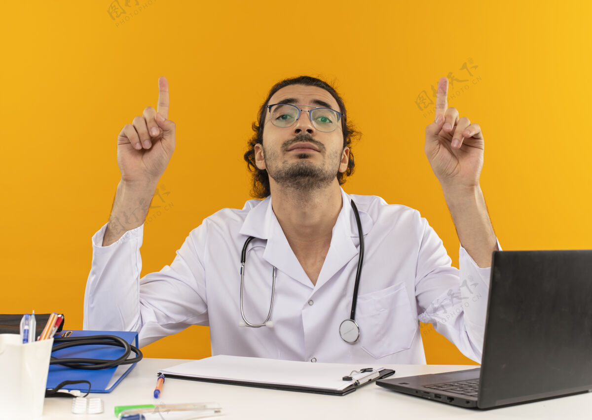医生年轻的男医生戴着医用眼镜 穿着医用长袍 听诊器坐在桌子旁穿长袍工作