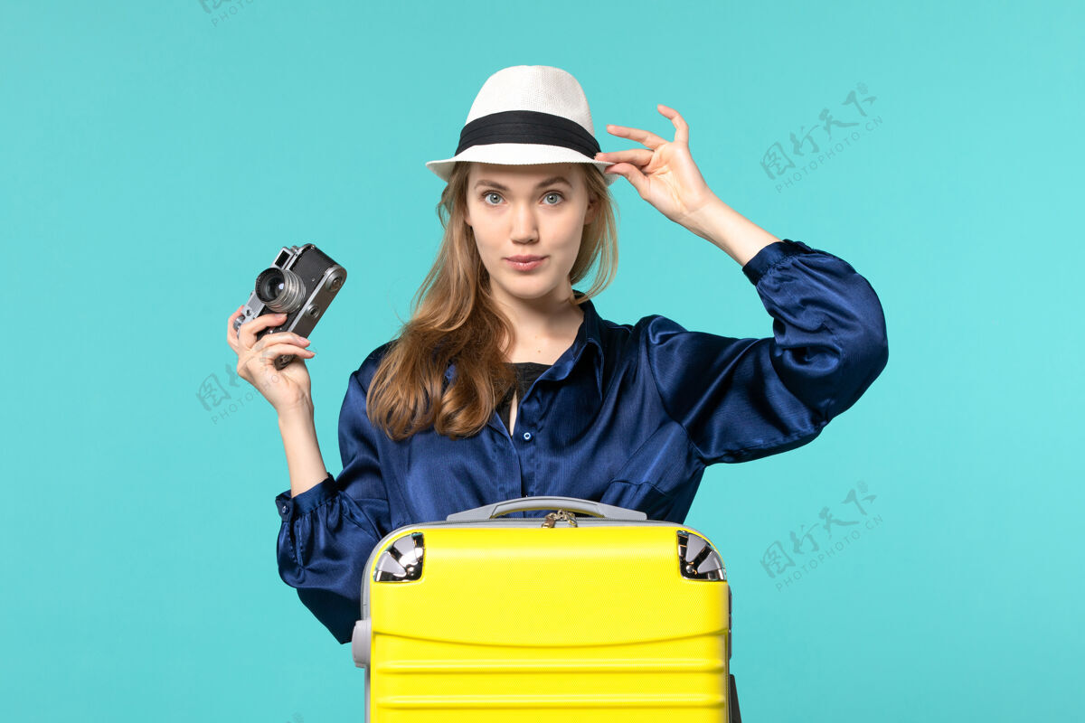 微笑前视图年轻女子拿着相机 在蓝色背景上摆姿势 女子远航海航飞机成人相机旅行