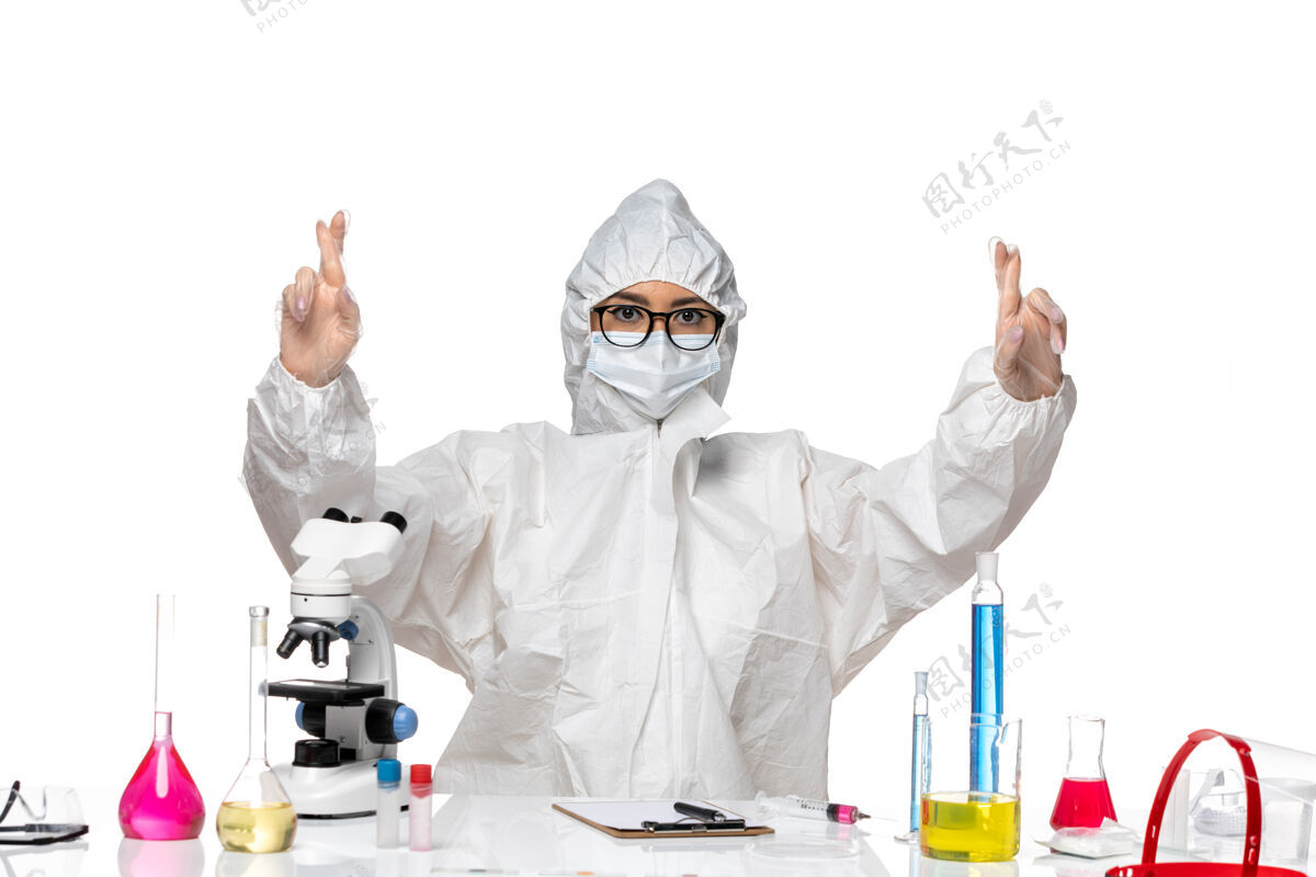 药正面图穿着特殊防护服的年轻女化学家坐在桌子前 白色办公桌上的解决方案病毒实验室可维健康化学套装坐姿外套
