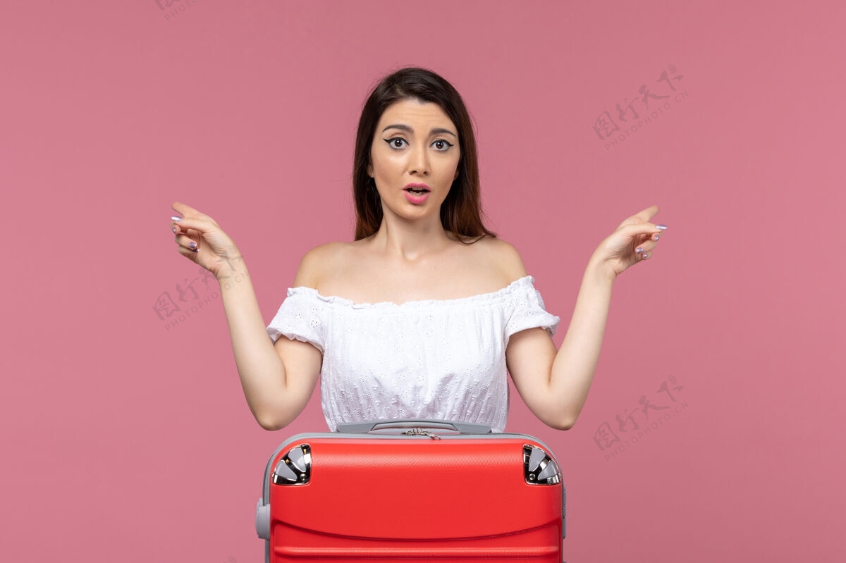 准备正面图：年轻女性带着她的红色袋子准备度假 背景是粉色的出国旅行和海上旅行包旅行旅行