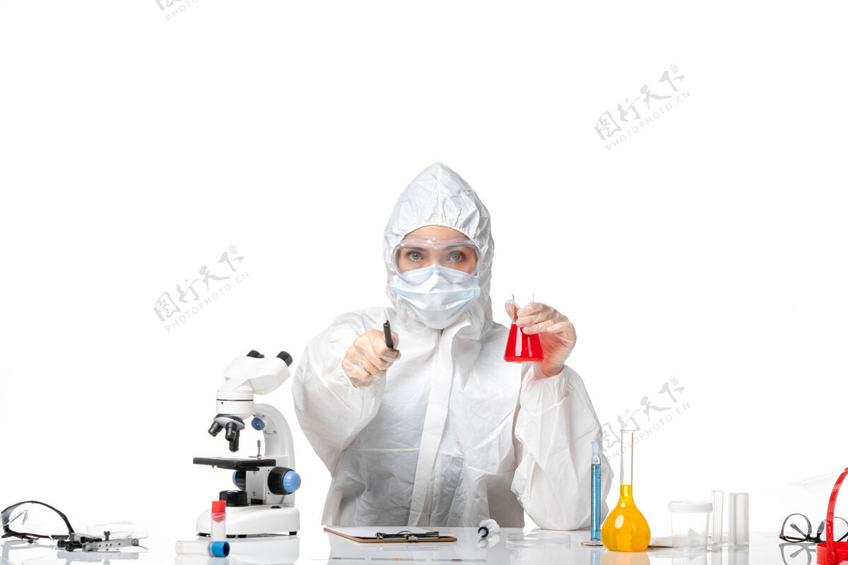 病毒正面图年轻女医生穿着白色防护服带口罩由于柯维德手持红色溶液在白色背景上飞溅病毒大流行柯维德-大流行解决方案套装