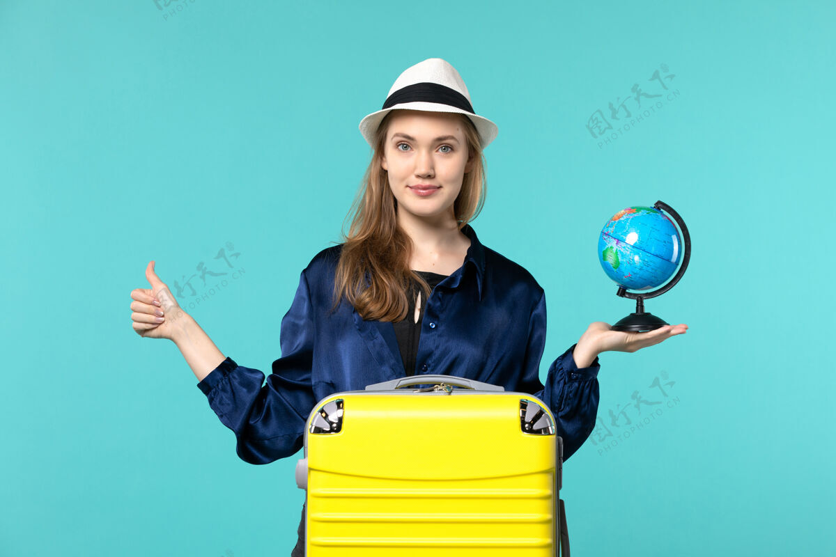 手持前视图年轻女子手持地球仪 准备在蓝色背景飞机上度假女性度假之旅旅程旅程成人