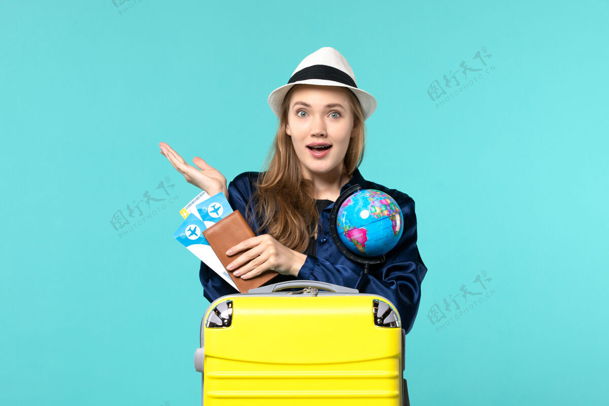 专业正面图年轻女子手持机票和地球仪上蓝色背景的飞机远航海上度假之旅肖像旅程票