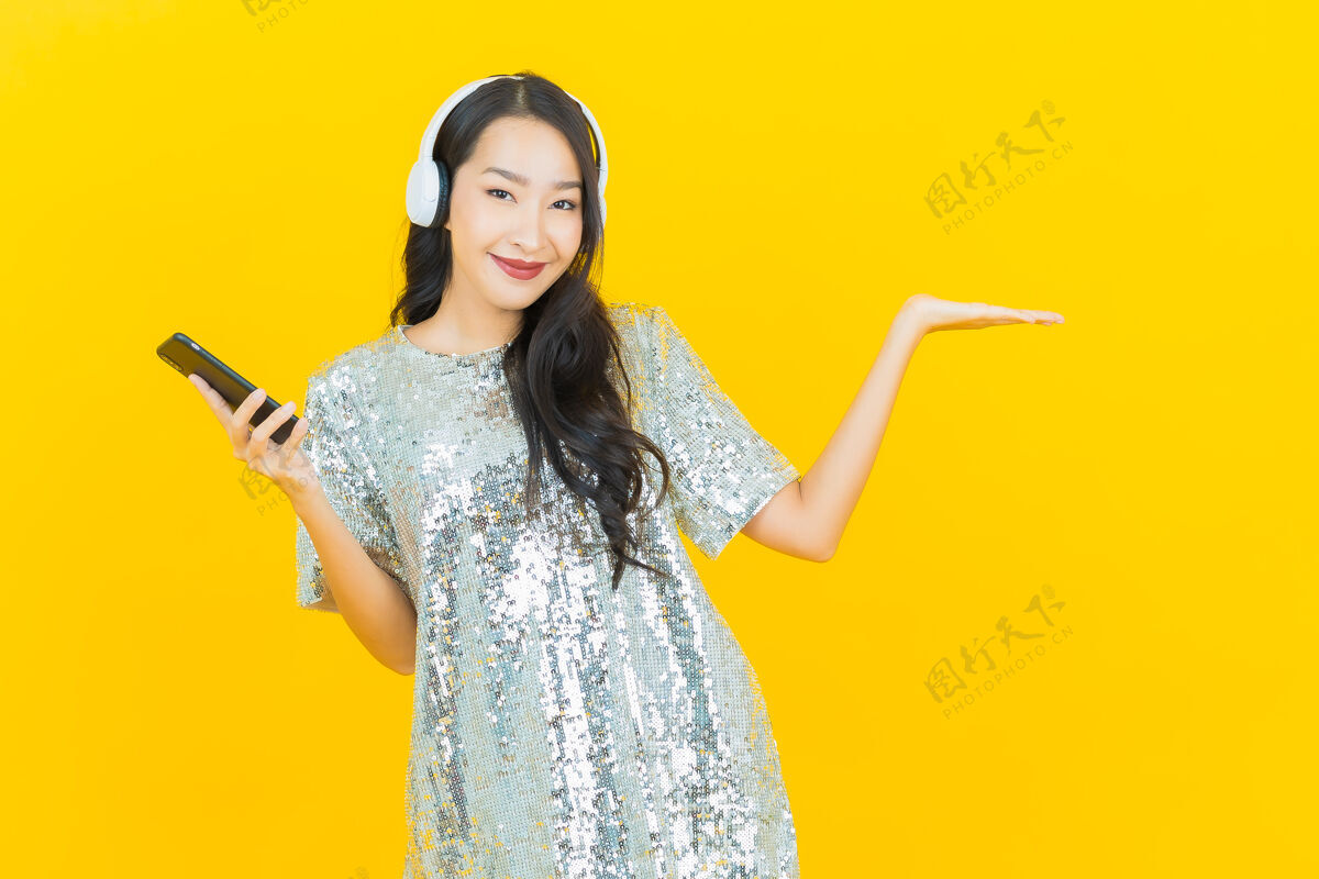 女人肖像美丽的亚洲年轻女子与耳机和智能手机听音乐的黄色成人年轻享受