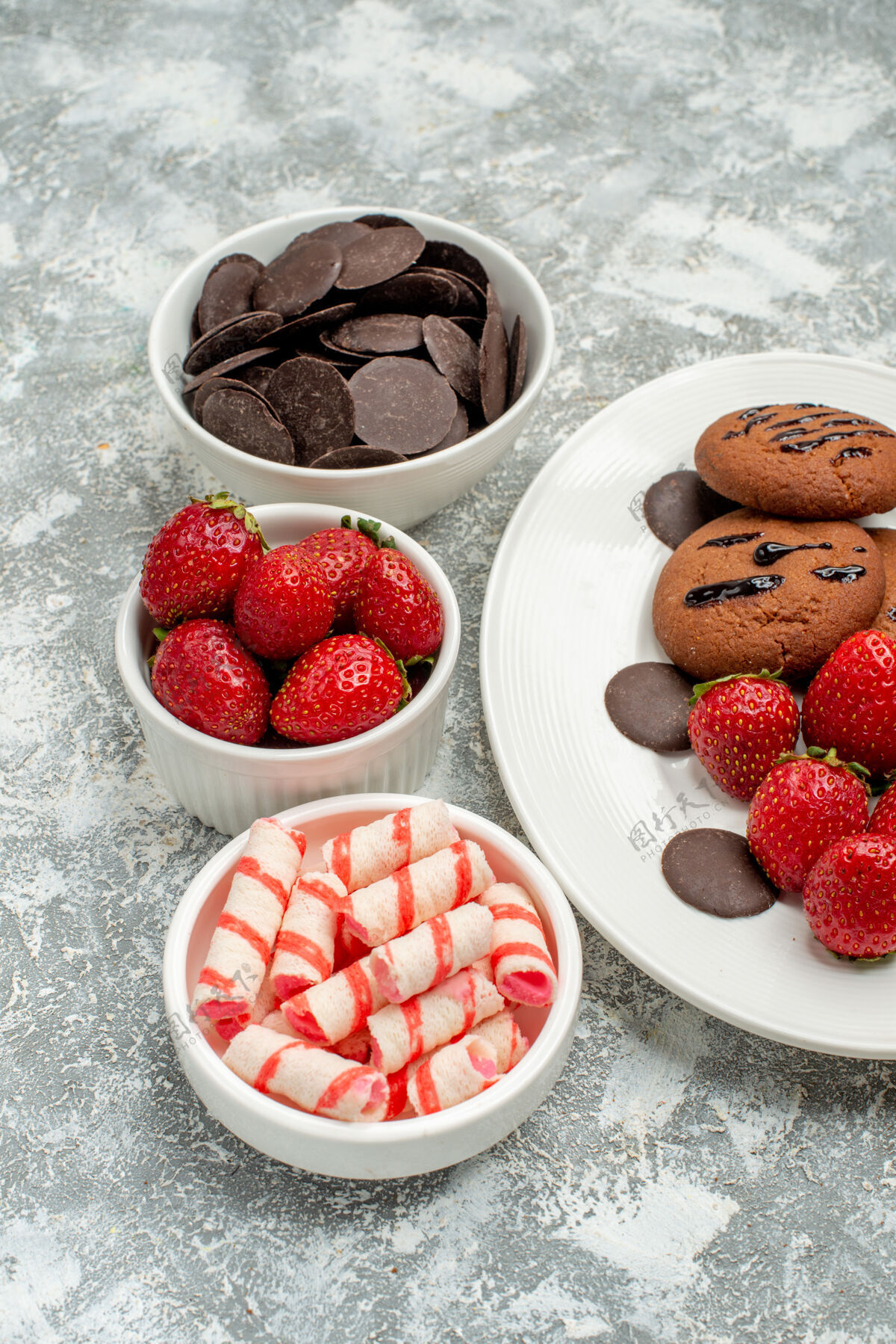 碗下半部分是白色椭圆形盘子上的巧克力饼干草莓和圆形巧克力 灰白色地面上的碗里有糖果草莓巧克力覆盆子糖果巧克力