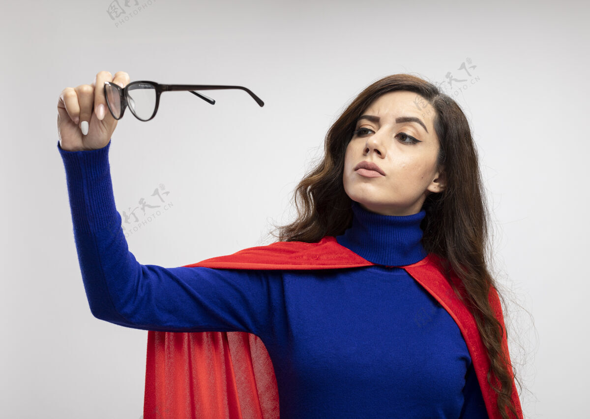 超级英雄自信的白种人超级英雄女孩 穿着红色斗篷 拿着白色的眼镜看自信斗篷眼镜