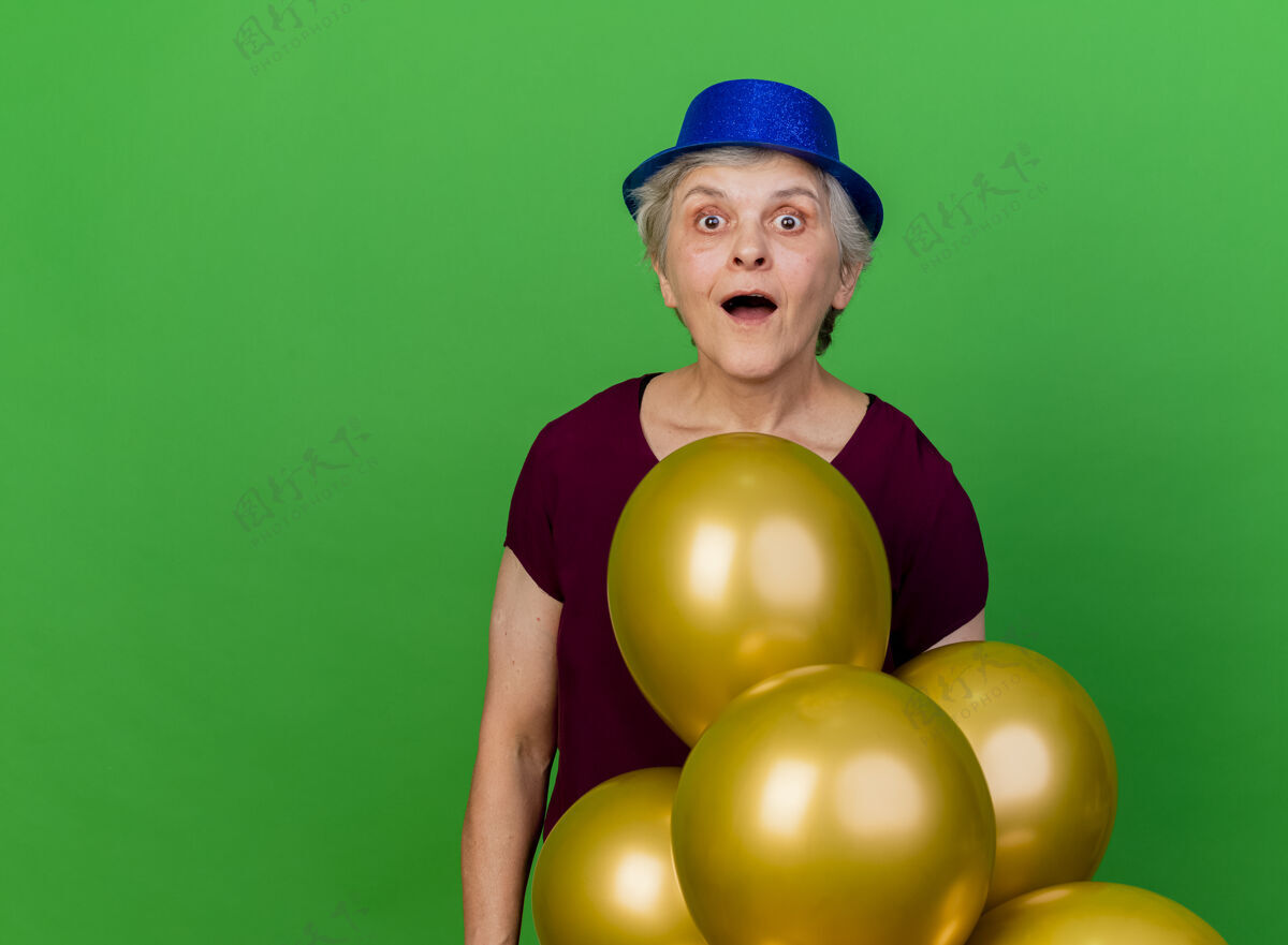 帽子兴奋的老妇人戴着聚会帽站在绿色的氦气球上派对兴奋老人