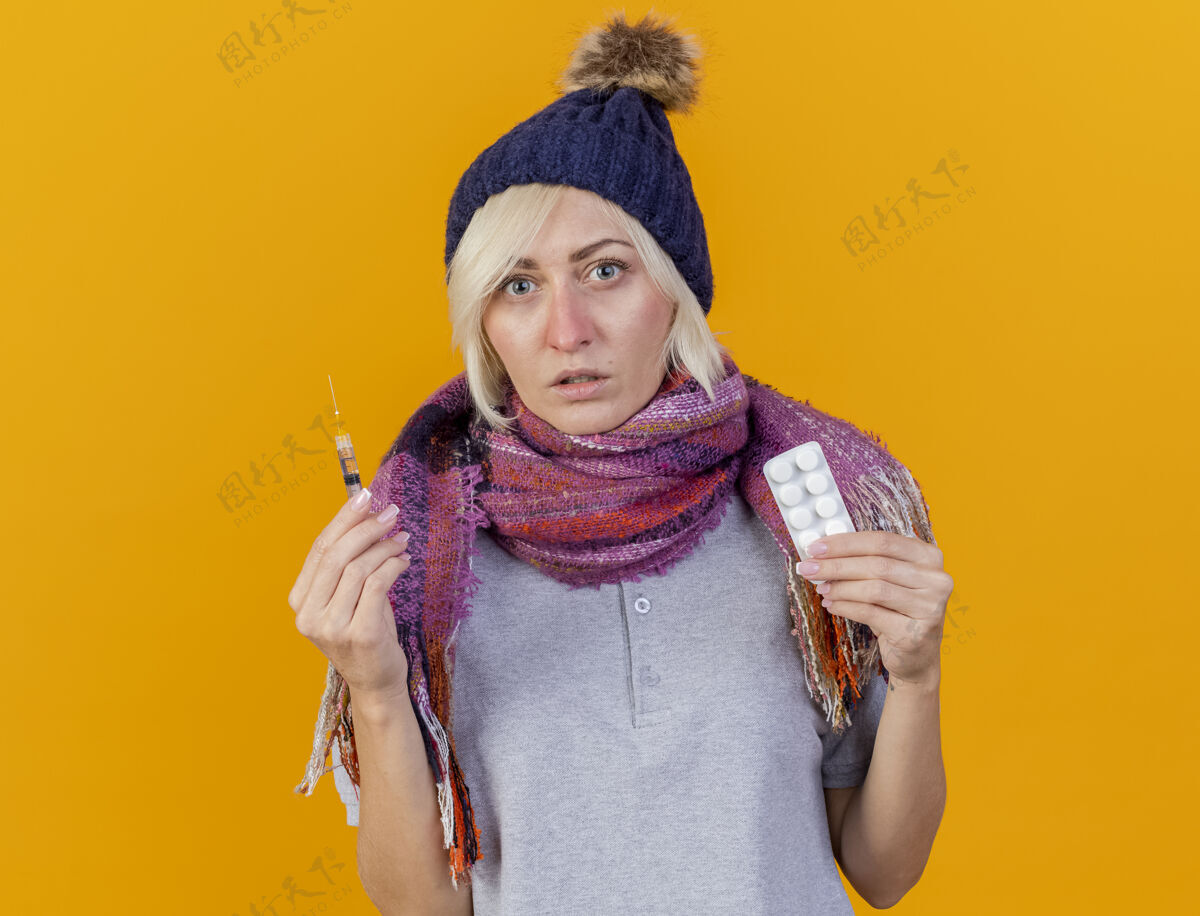 金发无知的年轻金发病斯拉夫妇女戴冬季帽子和围巾拿着注射器无知年轻人医生