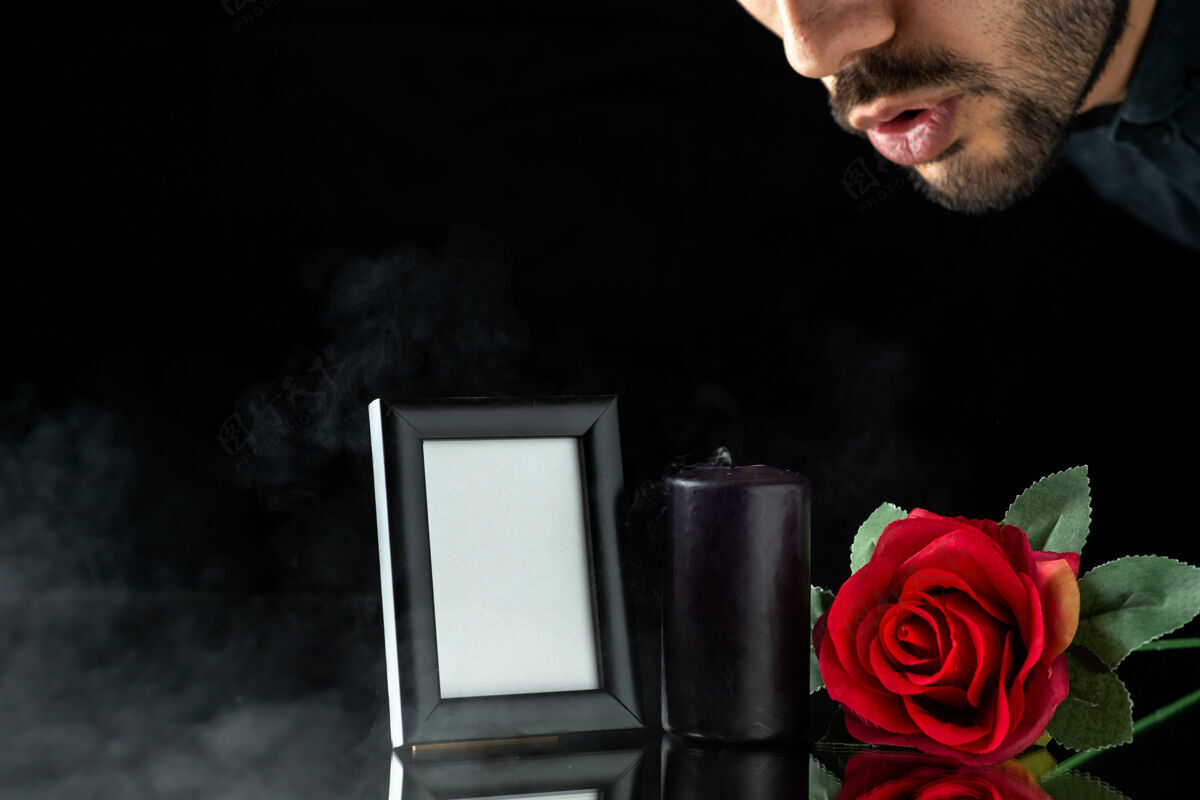 黑暗黑色表面上有红玫瑰和相框的深色蜡烛的正面图男人人物正面