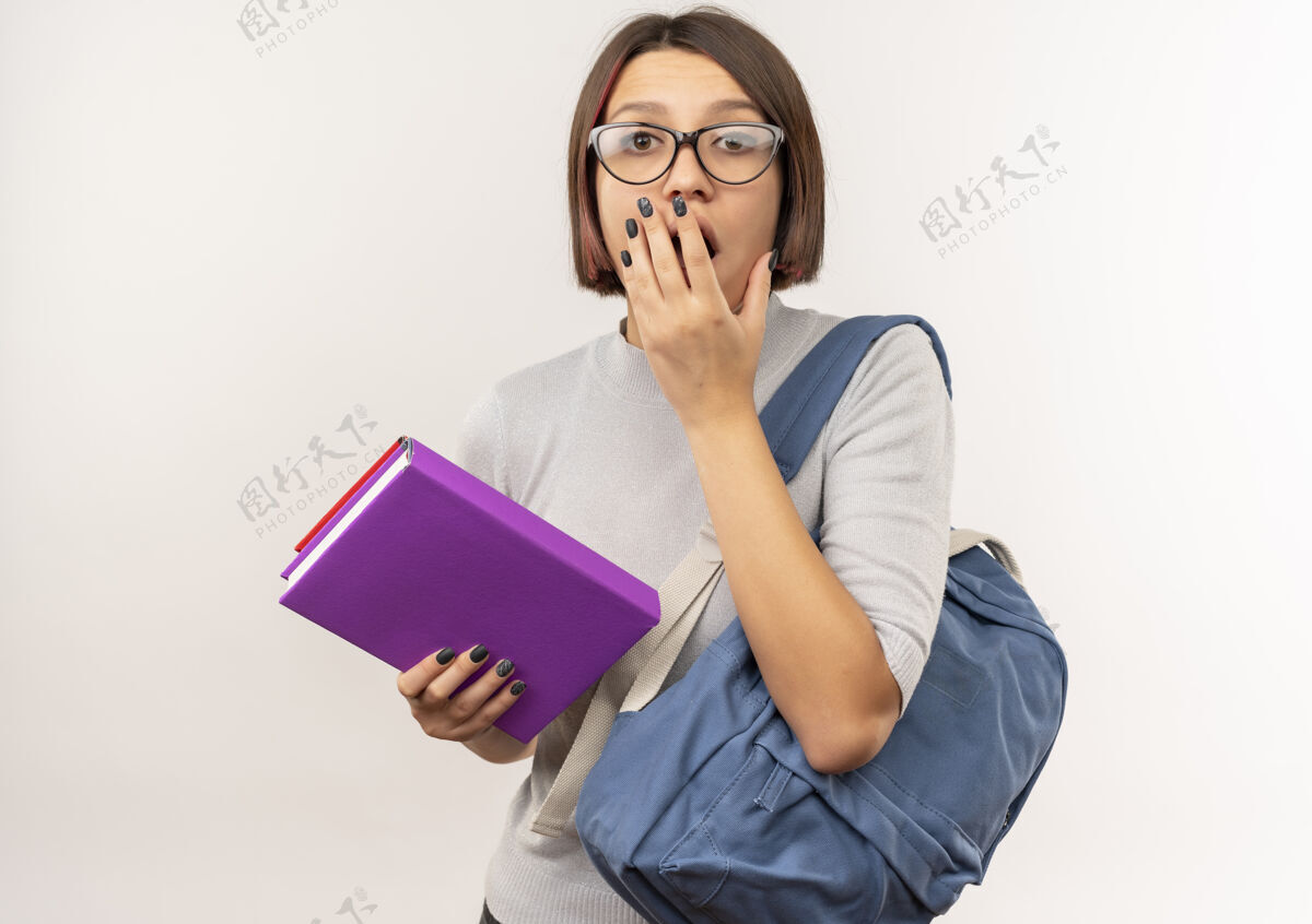 市民惊讶的年轻女学生戴着眼镜 背着书包 手放在嘴上 隔离在白墙上手表情年轻