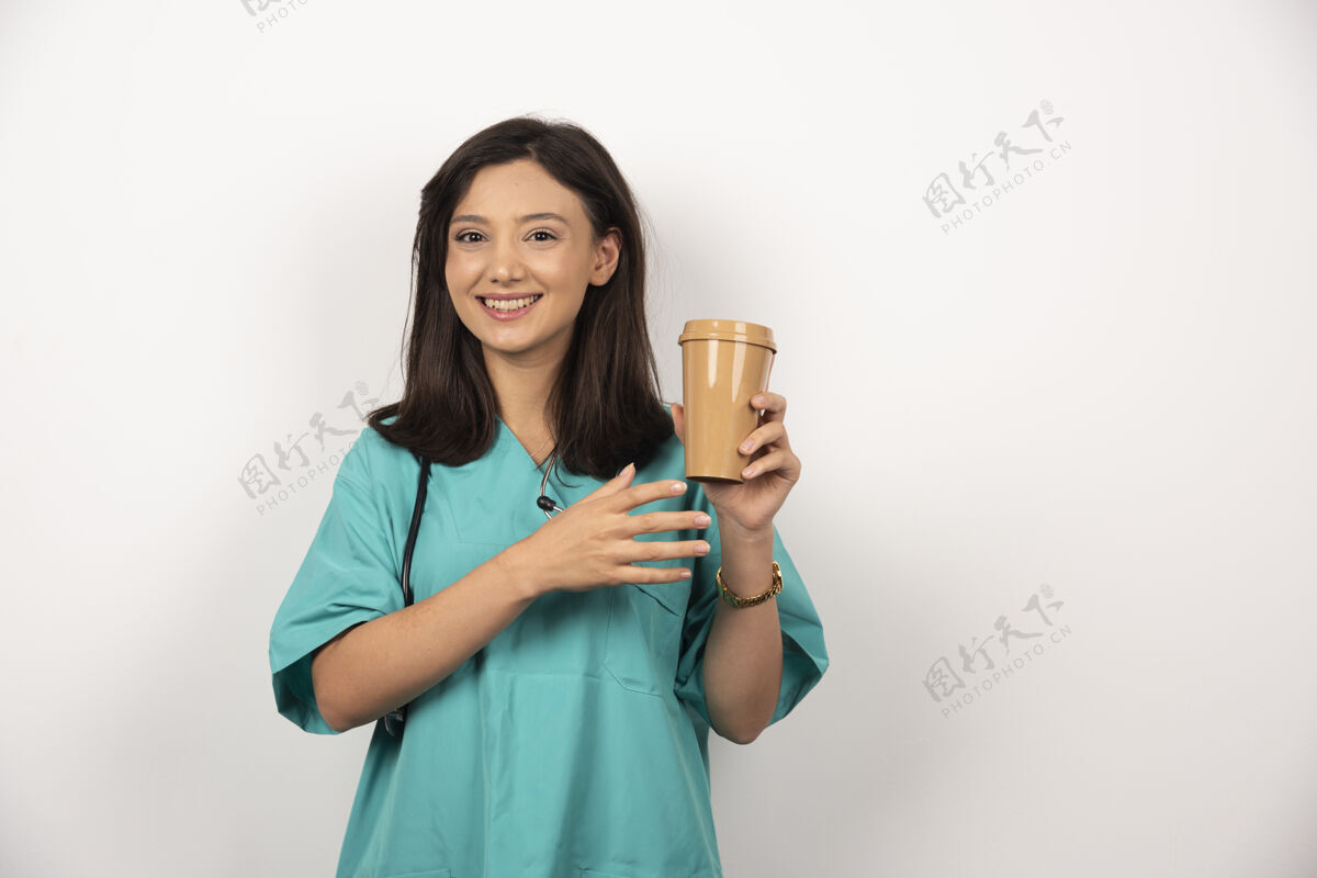 保健微笑的医生手持听诊器 在白色背景上端着一杯咖啡高质量的照片阳性医疗制服