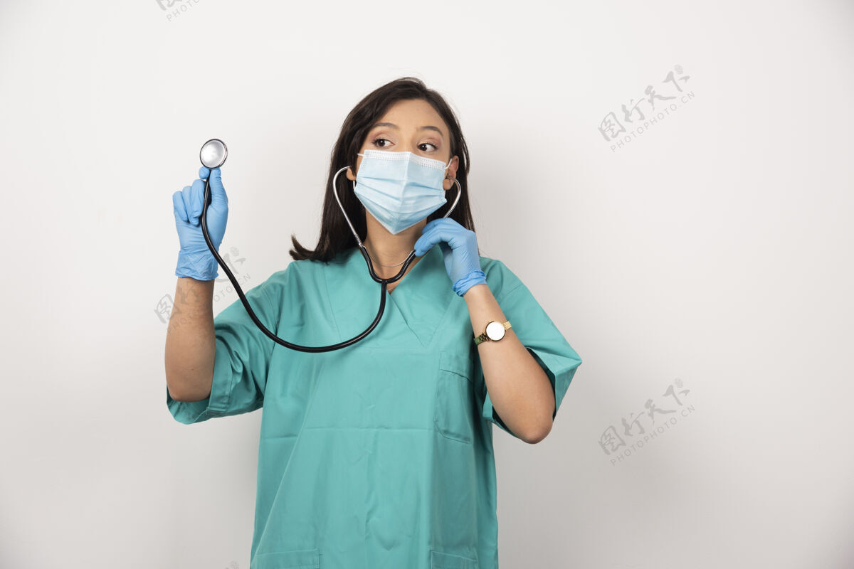 面罩戴着口罩的年轻医生在白色背景上使用听诊器高质量的照片医生制服女性