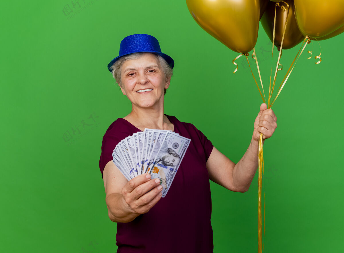 钱微笑着戴着派对帽的老妇人手里拿着钱 手里拿着氦气球女人老人派对