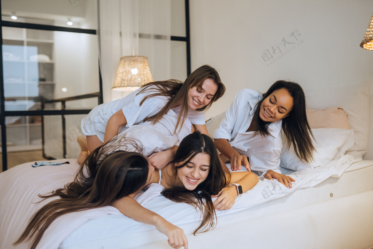 女性在家里的母鸡聚会上 积极的年轻女孩和女人朋友在床上放松睡衣女孩