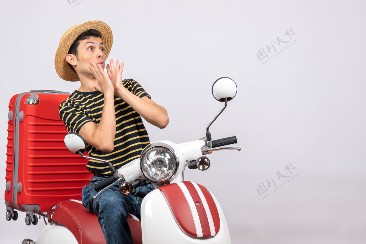 坐着骑着轻便摩托车戴着草帽的吓坏了的年轻人的正视图帽子传送带车辆