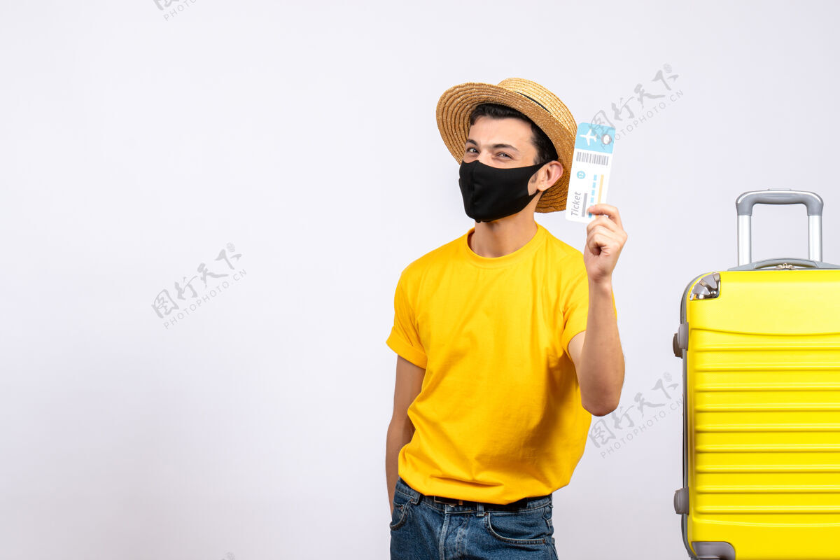 持有正面图身穿黄色t恤的年轻游客站在黄色手提箱旁举着旅行票人站立向上