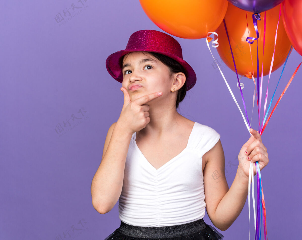 下巴困惑的年轻白种人女孩 戴着紫色派对帽 手里拿着氦气球 手放在下巴上 孤立地看着紫色的墙壁 还有复制空间气球女孩孤立