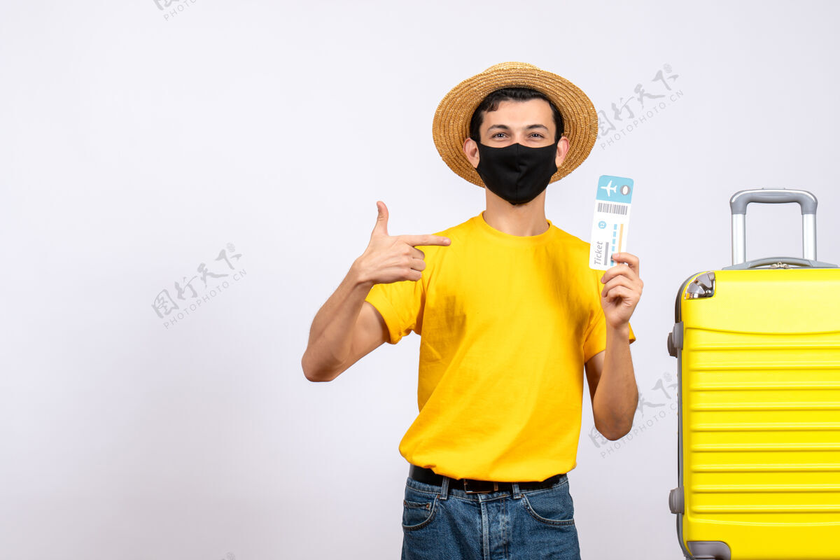 风景正面图穿着黄色t恤的年轻人站在黄色手提箱旁指着旅行票站着票T恤