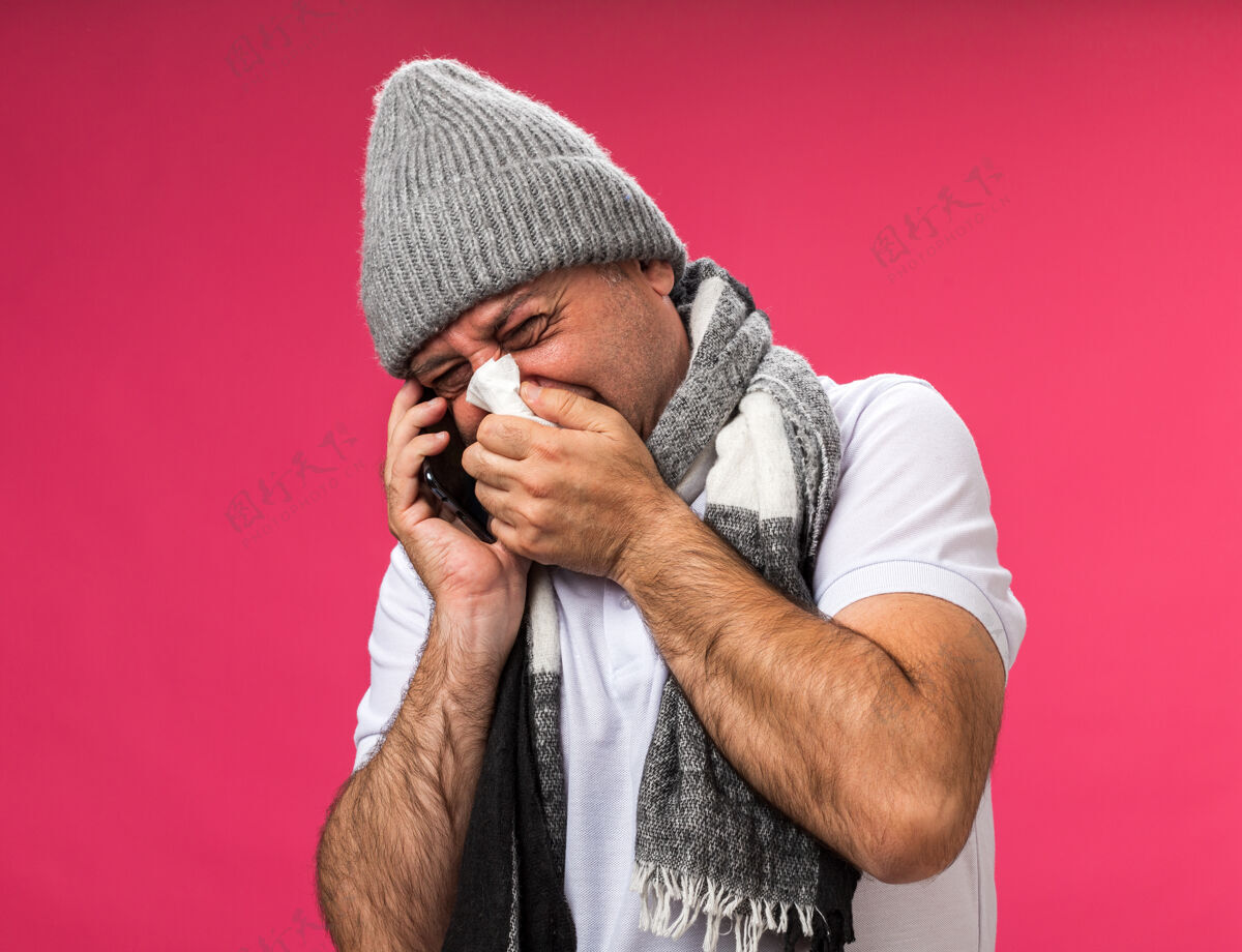 周围未经许可的成年白种人 脖子上围着围巾 戴着冬季帽子 用餐巾擦鼻子 讲电话 隔离在粉红色的墙上 留着复印空间成人不愉快餐巾