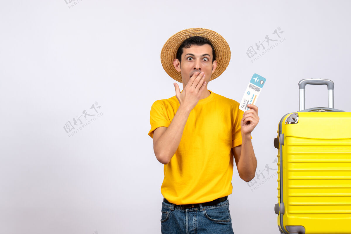 年轻人正面图：一个穿着黄色t恤的年轻人拿着票站在黄色手提箱旁边帽子前面成人