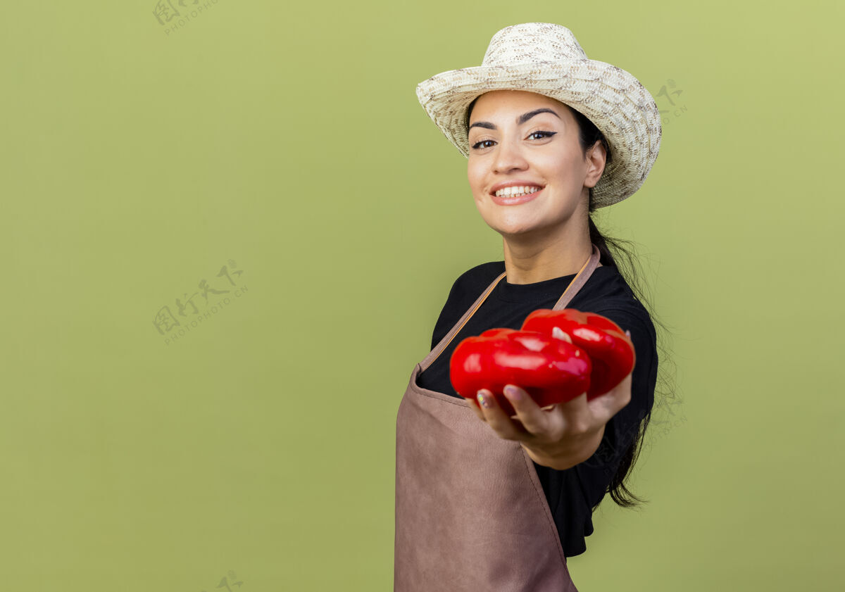 市民年轻漂亮的女园丁 围裙戴着帽子 站在浅绿的墙边 红灯笼椒在前面微笑着看着花园人脸